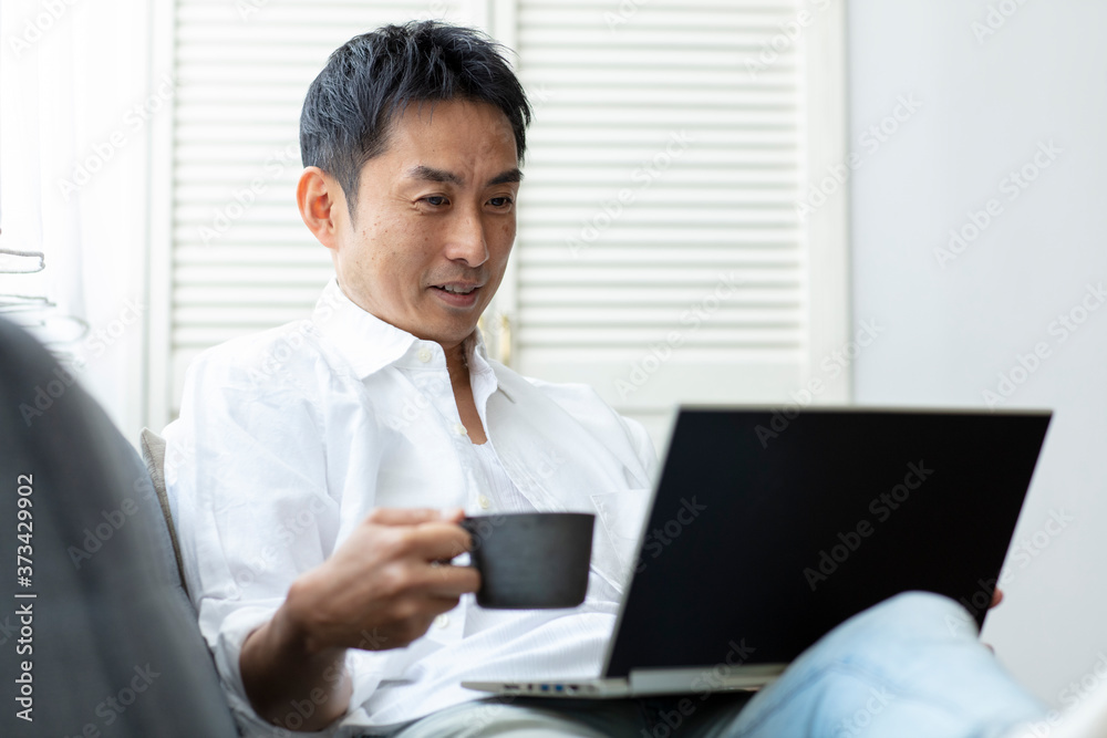 コーヒーカップを持ってノートパソコンを見る日本人男性 コーヒーカップを持ってノートパソコンを見る日本人男性