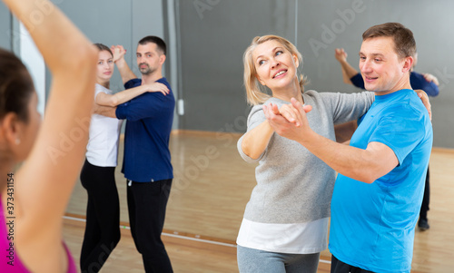 Cheerful middle aged woman learning to dance waltz with partner in dancing class