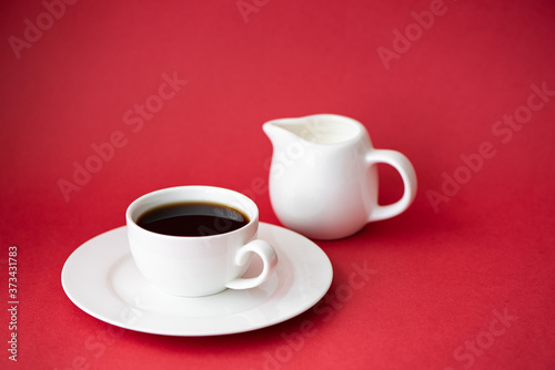 black coffee in small white coffee cup and milk jug on red background