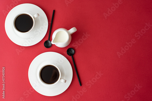 black coffee in small coffee cup and milk jug on red background