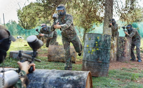 Paintball players aiming and shooting with guns at an opposing team outdoors