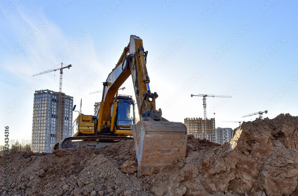 Excavator working at largest construction site. Backhoe on earthworks. Tracked loader laying external sewer pipes. Sewage drainage system. Tower cranes build high-rise buildings. Excavator working at largest construction site. Backhoe on earthworks. Tracked loader laying external sewer pipes. Sewage drainage system. Tower cranes build high-rise buildings.