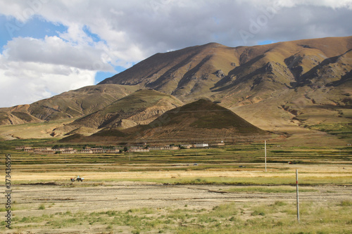 View of the mountains, barley field and Tibetan village with dramatic sky in Tibet, China 