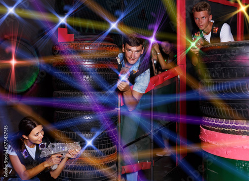 Group of positive friends playing laser tag game with laser guns near tires in labyrinth