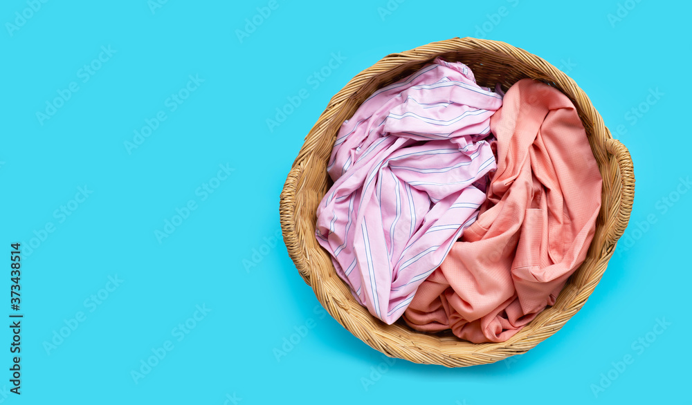Fototapeta premium Colorful clothes in laundry basket on blue background.