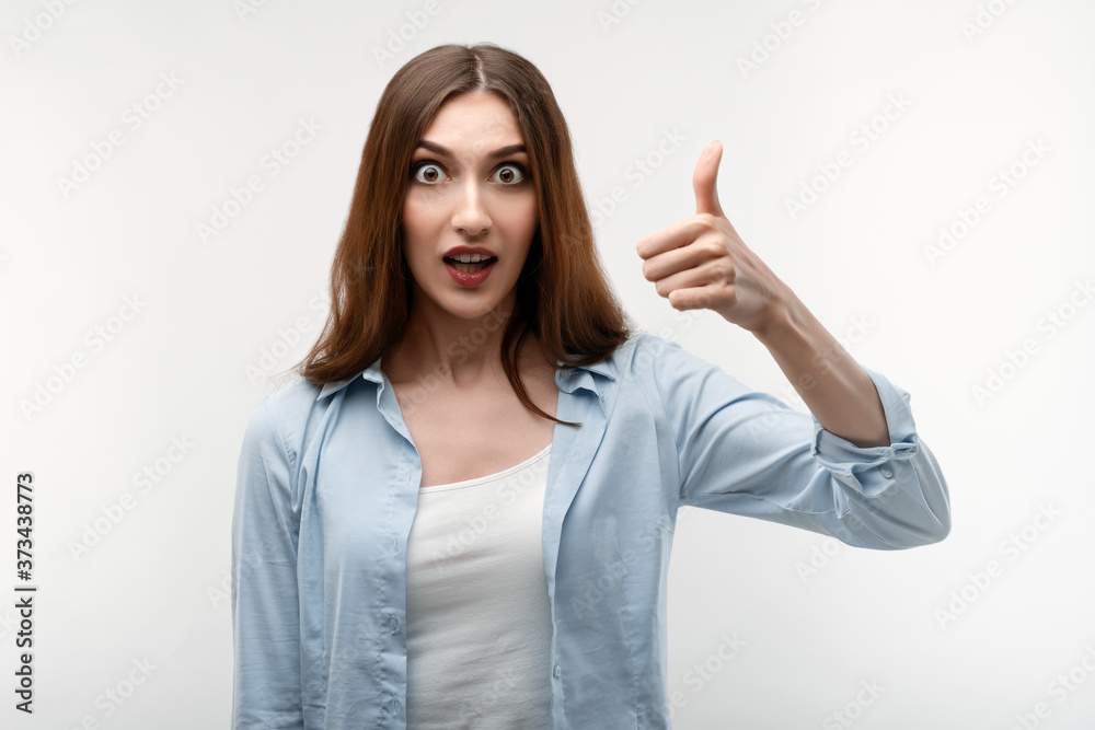 Caucasian Young female with long chestnut hair, dressed in casual clothes, shows OKAY sign, demonstrates approval Caucasian Young female with long chestnut hair, dressed in casual clothes, shows OKAY sign, demonstrates approval