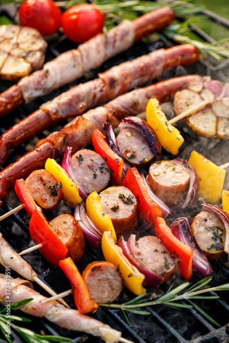 Grilled food, skewers and sausages wrapped in bacon with aromatic herbs on cast iron grill top view