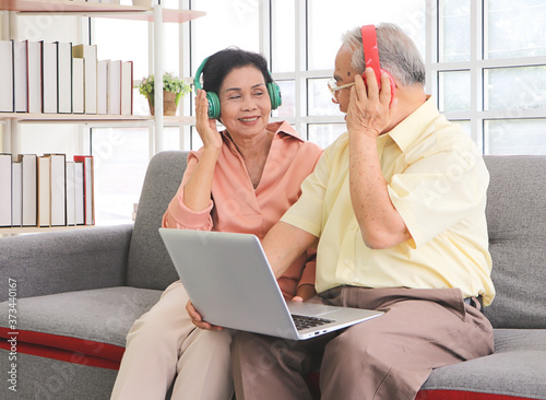 фотографія Asian senior couple having goodtime together , listen to the music from headphones with computer laptop on lap