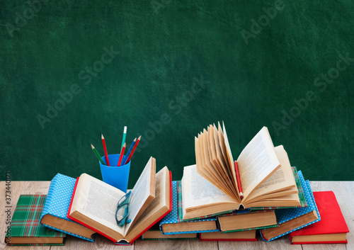 Back to school, pile of books in colorful covers and on wooden table with empty green school board background. Distance home education.Quarantine concept of stay home.