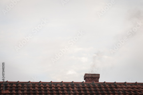 brick chimeny on the roof of an individual residential house with tiles exhausting little fumes at dusk, during a sunny afternoon
