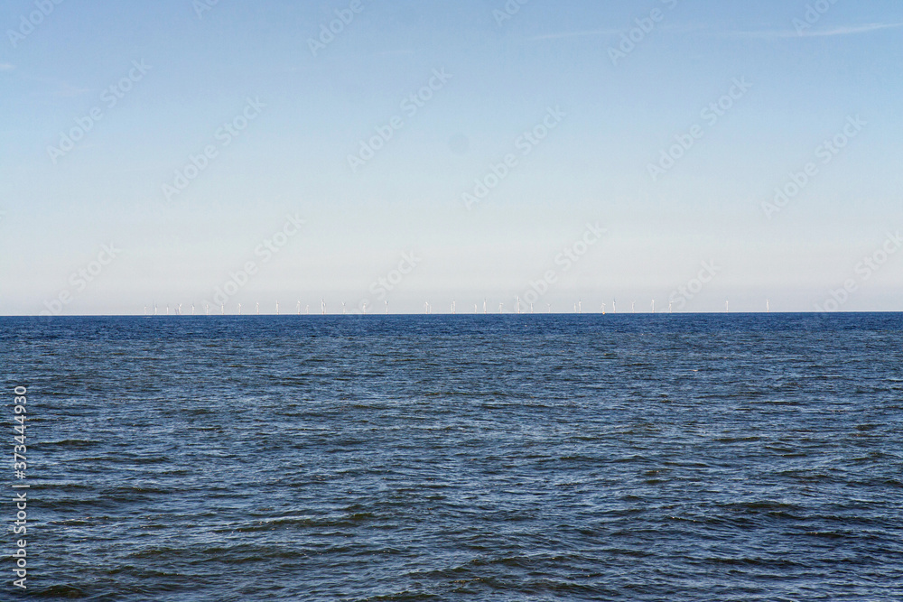 Obraz premium An offshore wind farm in the North Sea, barely visible on the horizon, just off the coast of the Netherlands, on a clear day.