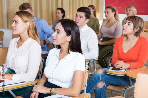 Portrait of young woman attentively listening to lecture in classroom full of students..