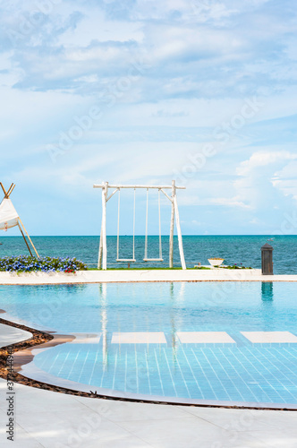 Swimming pool and white double swing and small pavilion with blue sky in summer.