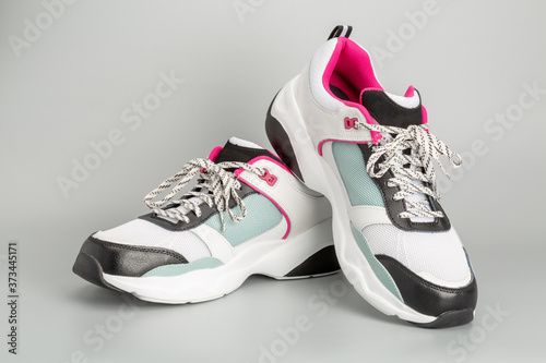 Weisse Damen-Sneaker mit hellblauen und rosaroten Akzenten. Mit grauem Hintergrund.