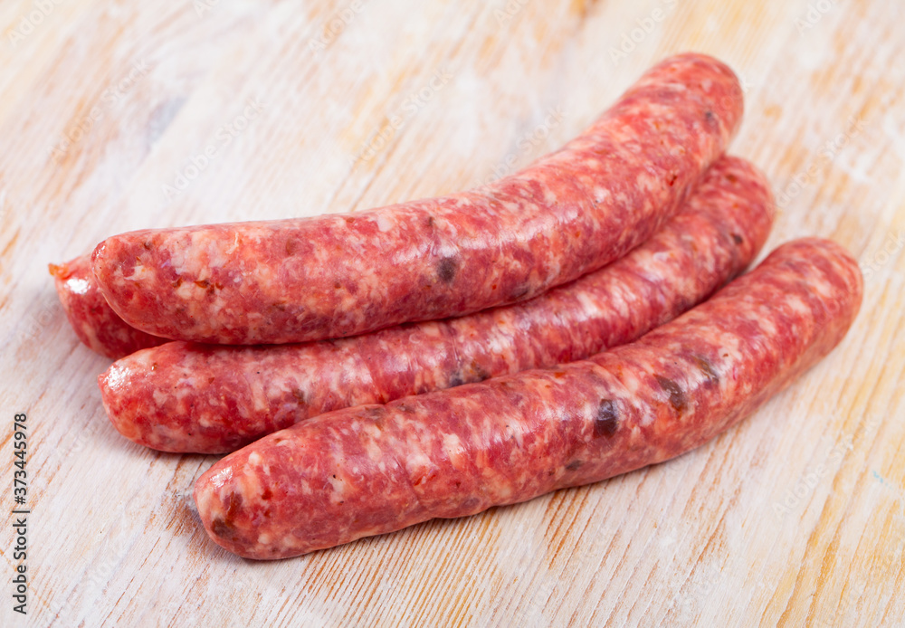 Raw sausages llonganissa prepared for barbecue on wooden background. Traditional Catalan meat products