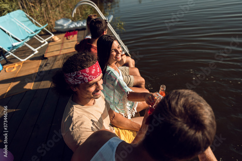 Group of young friends sitting on the edge of a pier having fun and enjoying a summer day at the lake.