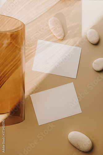 Blank paper sheet cards with empty copy space and tan glass tube with sunlight shadows on white background. Flat lay, top view business mock up template.