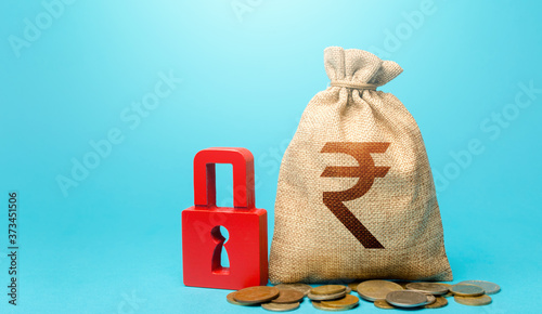 Indian rupee money bag and red padlock. Blocking bank accounts and seizing assets. Freezing of pension savings. Cash flow monitoring. Tight government control over the financial system.