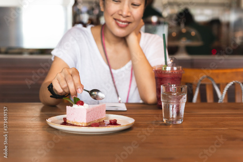 Happy woman eating currant mousse cake with spoon in cafe.