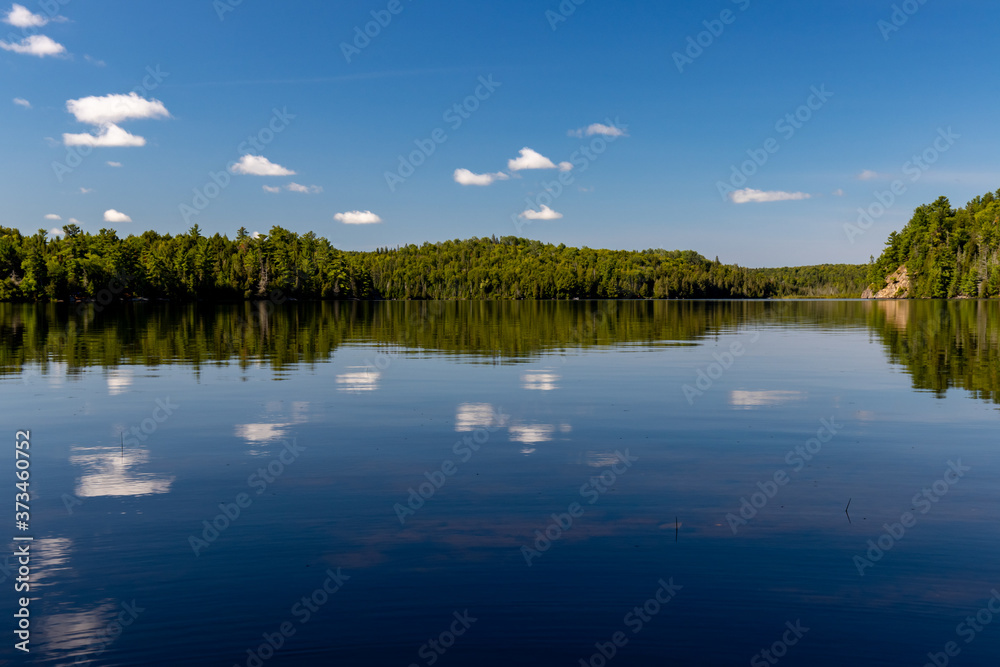 Serene Canadian lake landscape with white cloud reflections and blue sky
