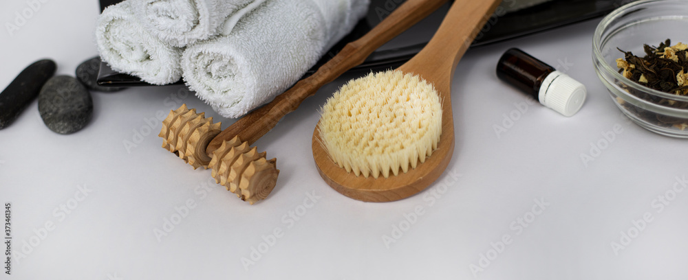 SPA Background for a banner with wellness items. Brush for dry body massage. Wooden massager for face and body. Wet white towels on a black ceramic dish. Sea pebbles and aromatic oil. Copy space SPA Background for a banner with wellness items. Brush for dry body massage. Wooden massager for face and body. Wet white towels on a black ceramic dish. Sea pebbles and aromatic oil. Copy space