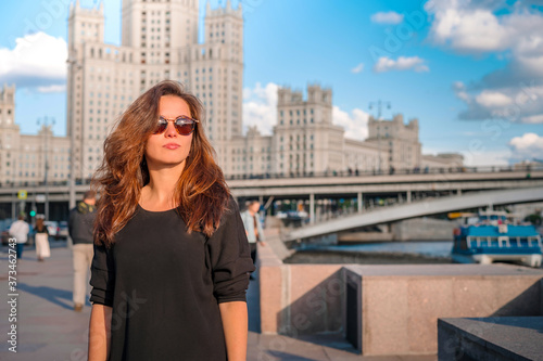 A young brunette woman walks in a tourist spot with the background of the famous high-rise and the Moscow river on a Sunny summer day