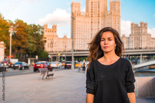 A young brunette woman walks in a tourist spot with the background of the famous high-rise and the Moscow river on a Sunny summer day