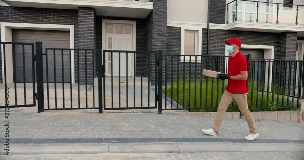 Caucasian young man courier in medical mask, hat and gloves walking the street and carrying carton parcel. Male delivery worker strolling with pizza box. Quarantine concept. Delivering. Coronavirus. Caucasian young man courier in medical mask, hat and gloves walking the street and carrying carton parcel. Male delivery worker strolling with pizza box. Quarantine concept. Delivering. Coronavirus.
