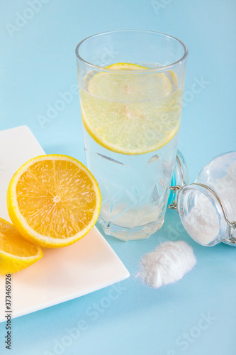 Baking soda in drinking glass with water and lemon slice juice, health benefits for digestive system concept. Light blue background.