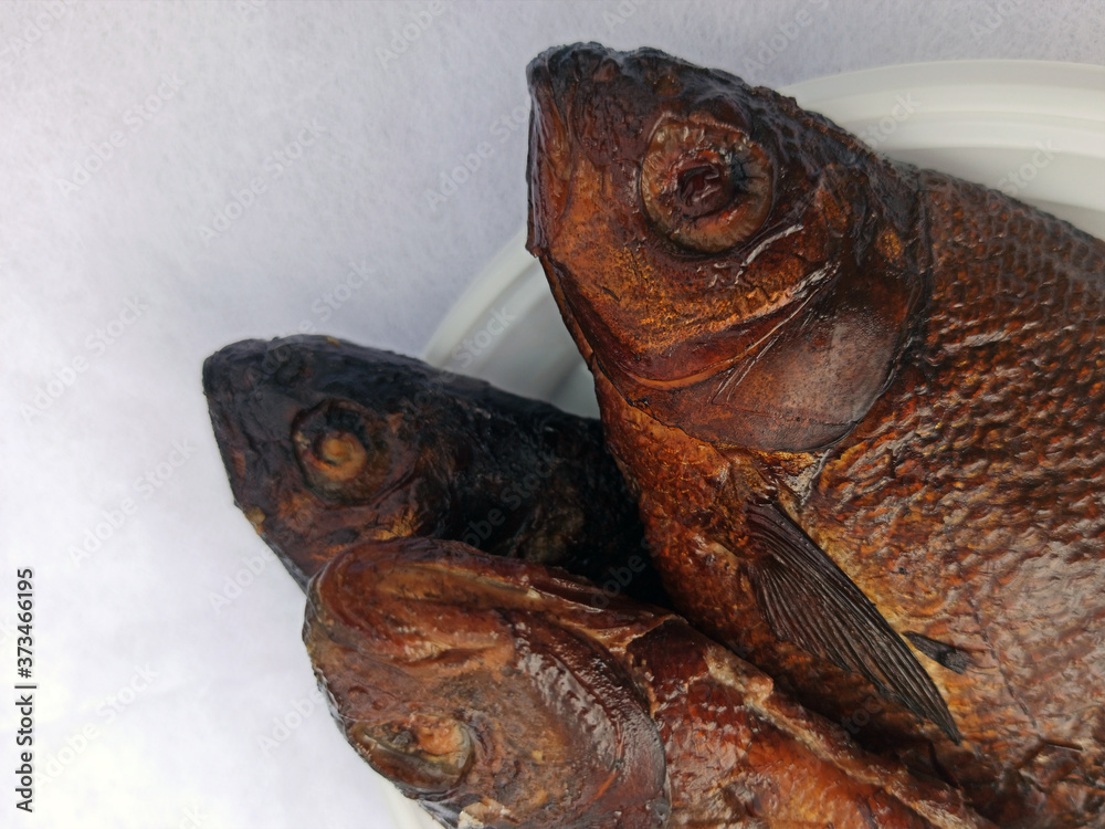 Smoked bream on a white plastic plate. Golden smoked fish close up top view. Hot smoked fish. Food photo.