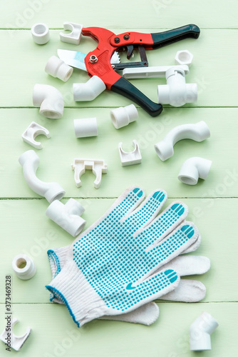 A pipe cutter and repair gloves lie along with plastic pipes on a wooden table.