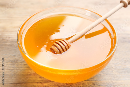 Tasty honey in glass bowl on wooden table, closeup