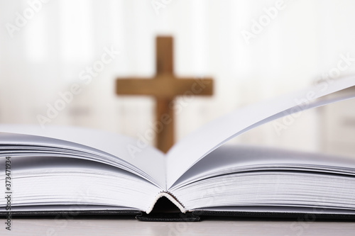 Open Bible on table and blurred cross on background, closeup. Christian religion © New Africa