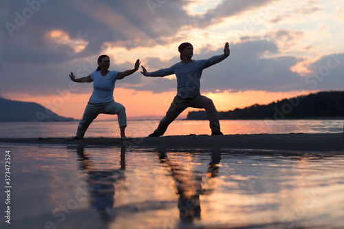 Man and woman doing Tai Chi chuan at sunset on the beach.  solo outdoor activities. Social Distancing. Healthy lifestyle  concept.  photo