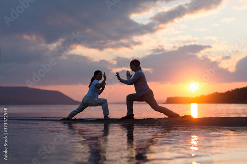 Man and woman doing Tai Chi chuan at sunset on the beach. solo outdoor activities. Social Distancing. Healthy lifestyle concept. 