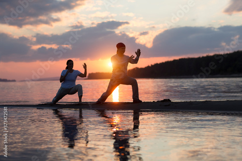 Man and woman doing Tai Chi chuan at sunset on the beach. solo outdoor activities. Social Distancing. Healthy lifestyle concept. 