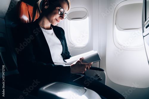 Bilde på lerret Adult delighted woman reading book in modern airplane