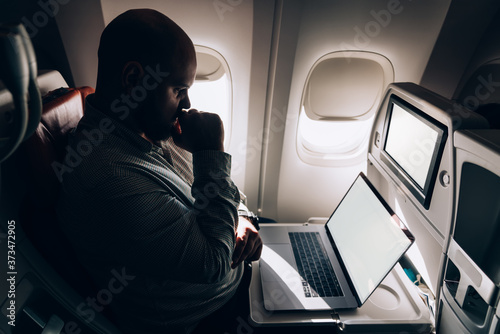 Thoughtful businessman using laptop in airplane