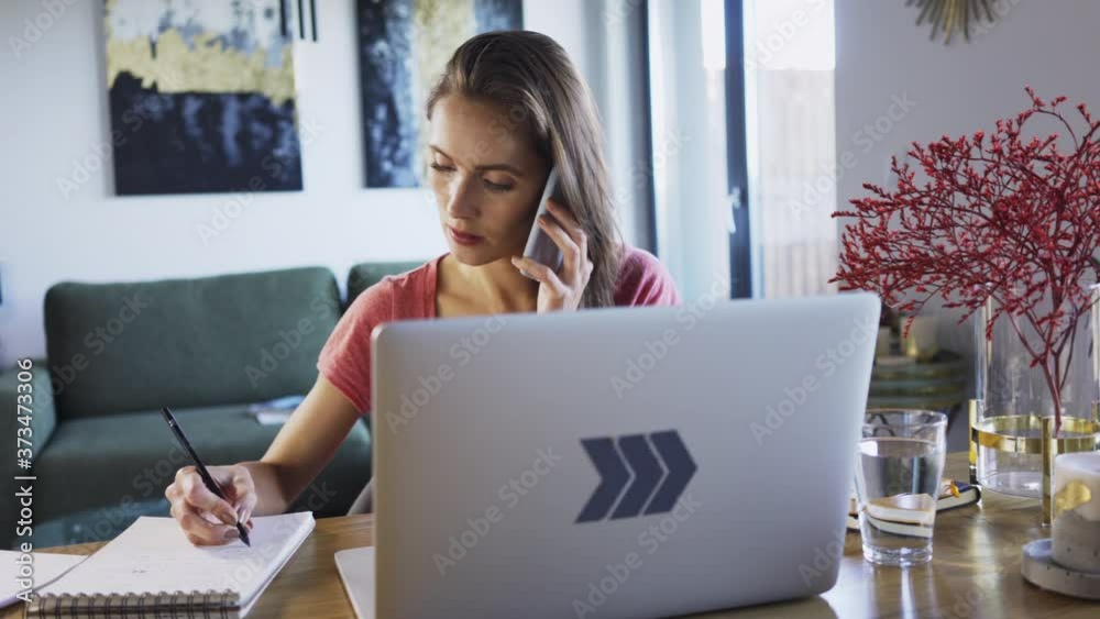 Woman working from home doing notes and talking on the phone