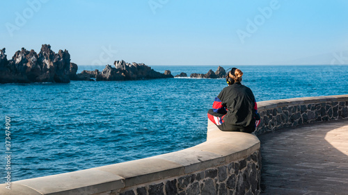 woman with headphones listening to music sitting by the ocean in