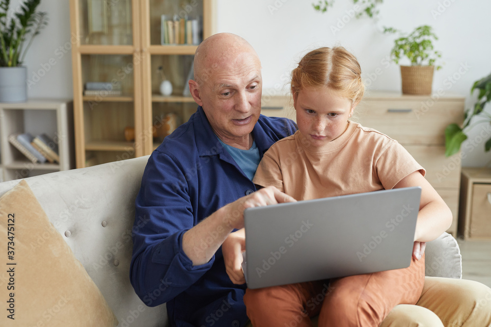 Warm toned portrait of happy grandfather using laptop with cute little girl in cozy home interior, copy space Warm toned portrait of happy grandfather using laptop with cute little girl in cozy home interior, copy space