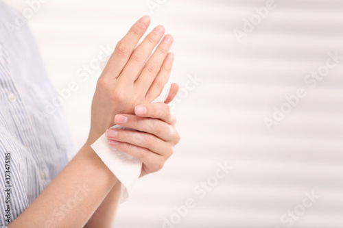 Woman cleaning hands with paper tissue on light background, closeup. Space for text