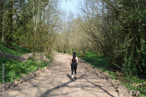 A young brunette woman standing on a wide woodland trail path on a walk in the sunshine