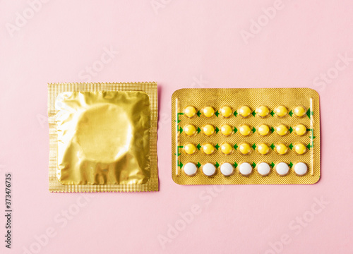 World sexual health or Aids day, condom in wrapper pack and contraceptive pills blister hormonal birth control pills, studio shot isolated on a pink background, Safe sex and reproductive health 