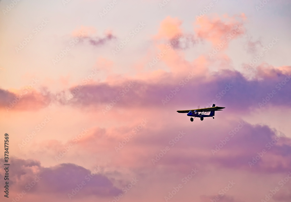 silhouette of ultralight microlite aircraft flying with a pilot and a passenger against sunset sky. silhouette of ultralight microlite aircraft flying with a pilot and a passenger against sunset sky.