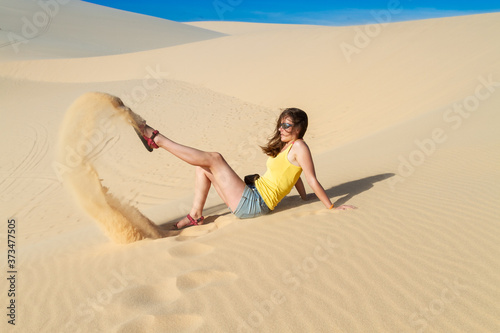 Woman sits on the sand in the desert, wearing a T-shirt and shorts. Playing with sand.