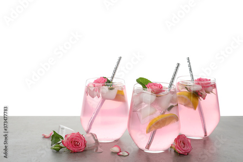 Delicious refreshing drink with rose flowers and lemon slices on light grey table against white background