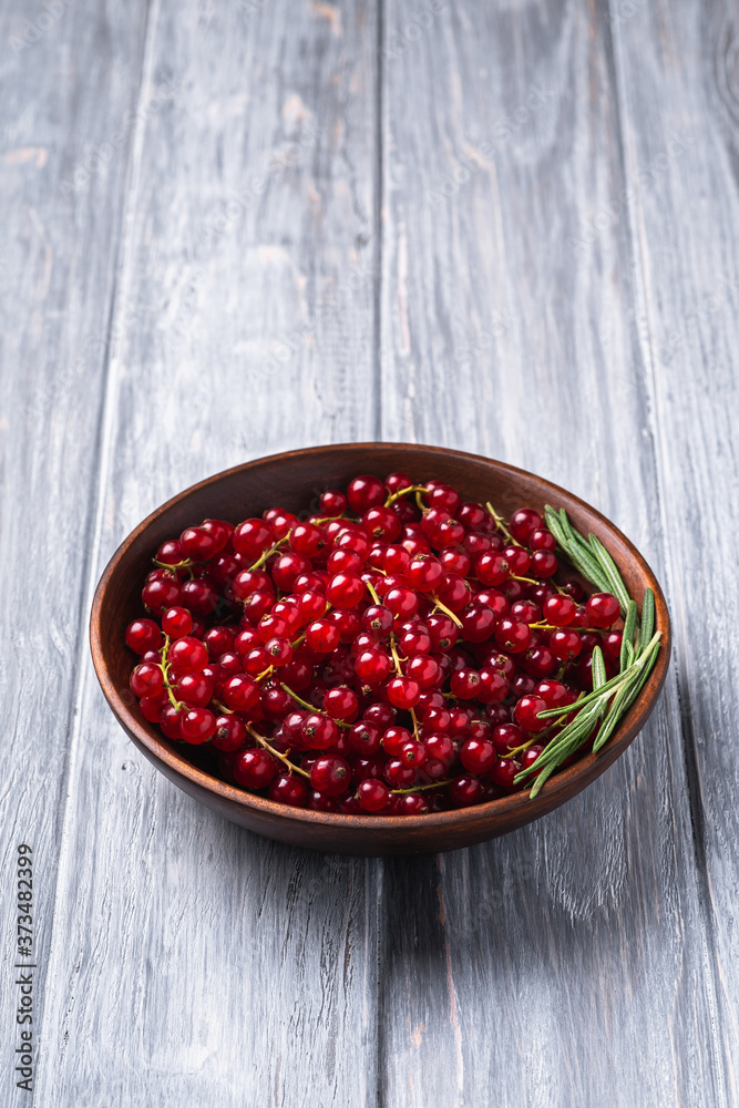Fresh sweet red currant berries with rosemary leaves in wooden bowl, grey wood background, angle view Fresh sweet red currant berries with rosemary leaves in wooden bowl, grey wood background, angle view