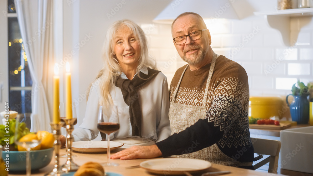 Happy Senior Couple in Love Have Romantic Evening, Smiling on Camera and Celebrating Anniversary. Elderly Have Romantic Evening with Wine, Festive Table in Cozy Kitchen Interior