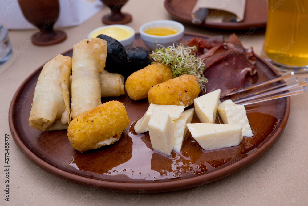 Beer snacks on a clay plate: bastruma, feta cheese, cheese in batter, honey and mustard. Soft focus.